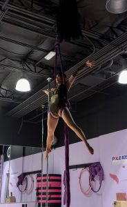 Amy, a student at pole kisses, positioned in a star hold on aerial silks.