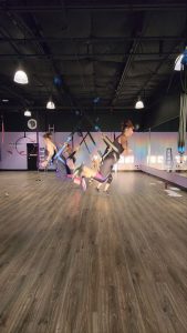 Students in a bungee fitness class jump between each other. Students are in a harness with bungee cords attached to the ceiling. 