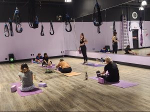 Students are stretching in a flexibility class with an instructor standing in the front. 